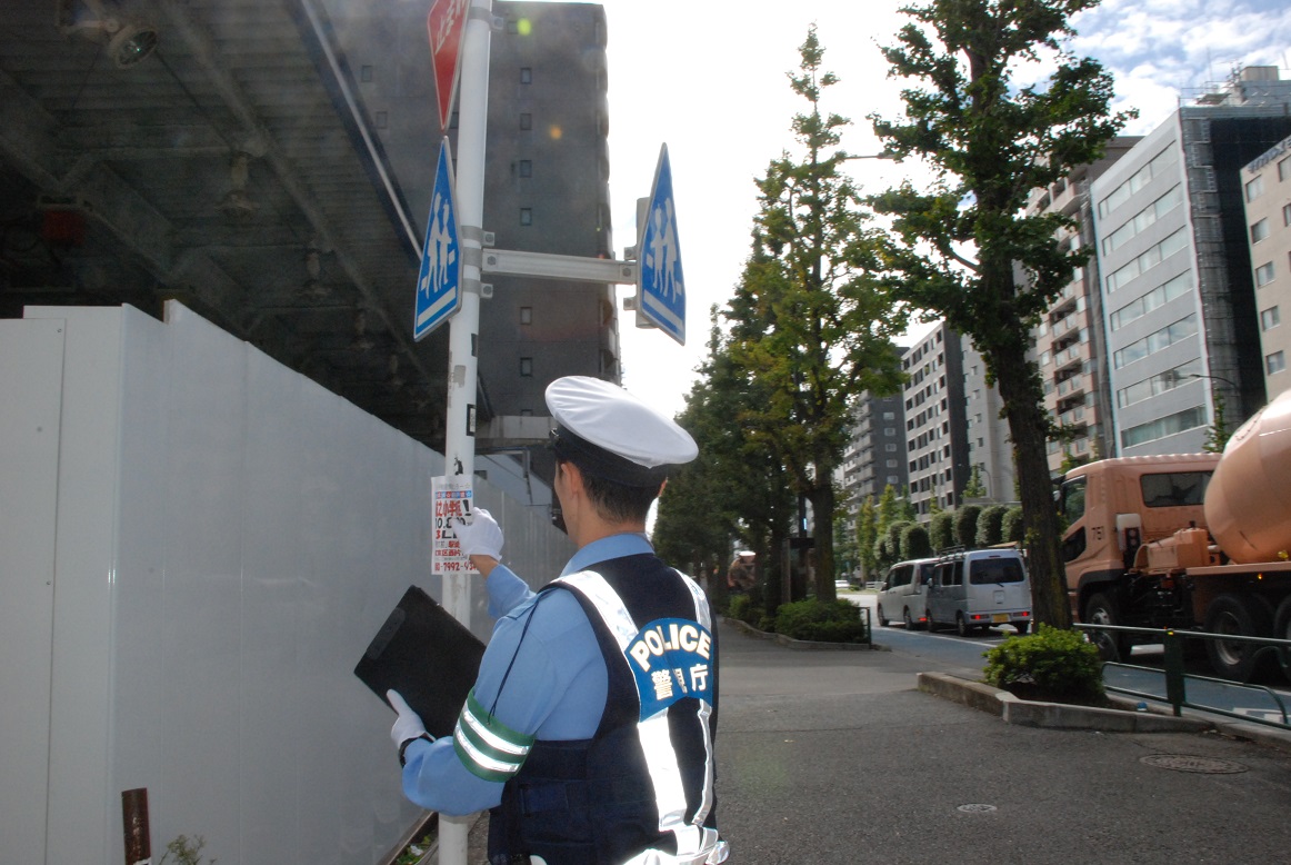 標識に貼られた違反広告物を除去する警察官